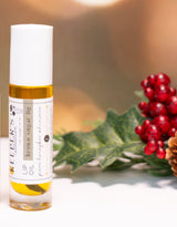 One small bottles with labels on a white surface with a festive background featuring berries and pine cones.