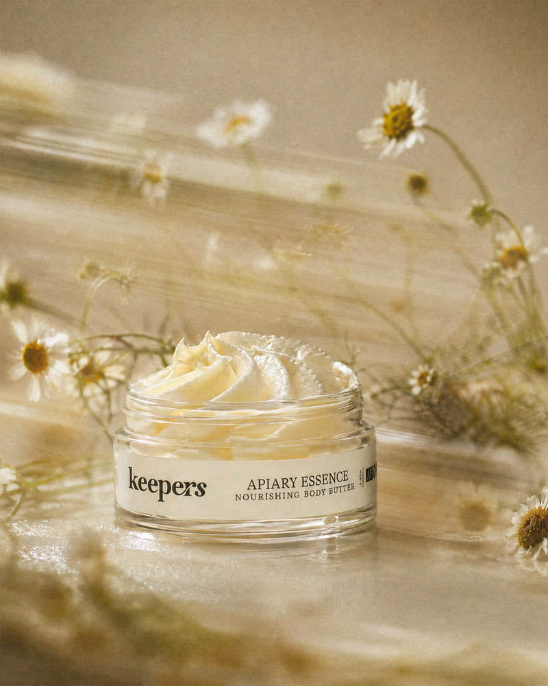 Jar of 'keepers Apiary Essence' body butter with flowers in the background