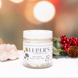 Jar of 'Keeper's Collective' whipped body butter with festive decorations on a blurred background